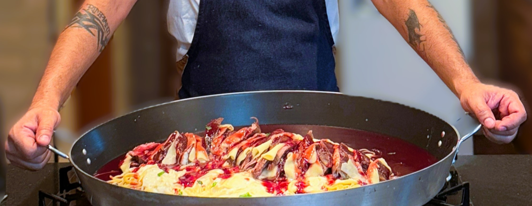 Personal chef Rafael Madeira com paellera de massa e carne na cozinha de casa