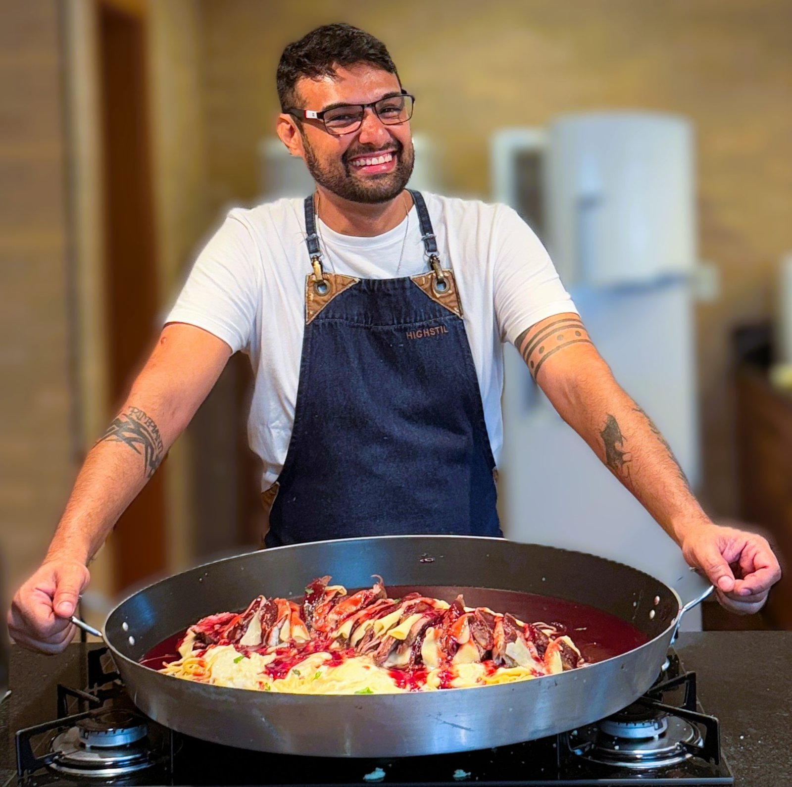 Chef com paellera de massa e carne em atendimento em casa