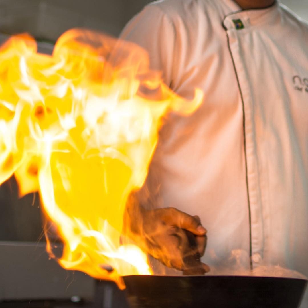 Close do flambado com o dólmã do Chef ao fundo